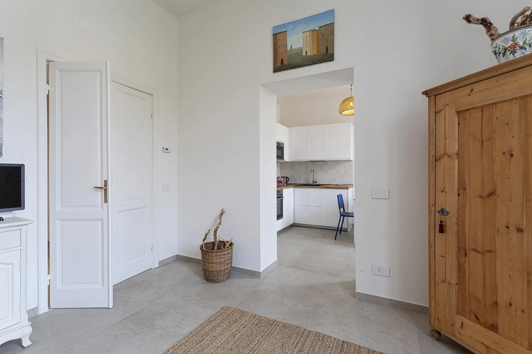 Una habitación luminosa se abre a una cocina blanca, con una cesta tejida cerca.