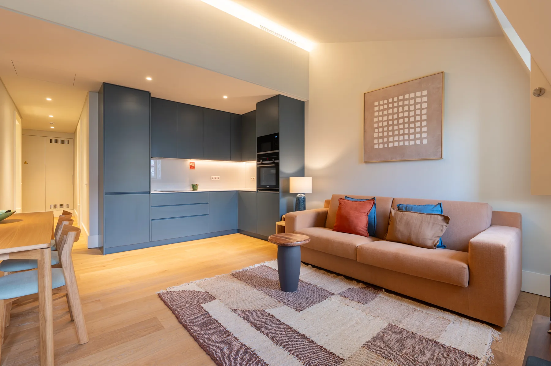 A living room with seating, a rug, and a kitchen area.