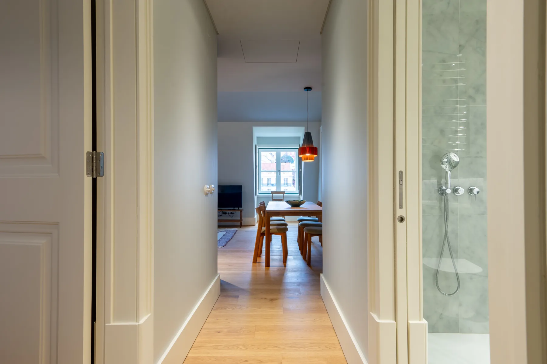 A hallway opens onto a dining area, with a glass shower visible beside it.