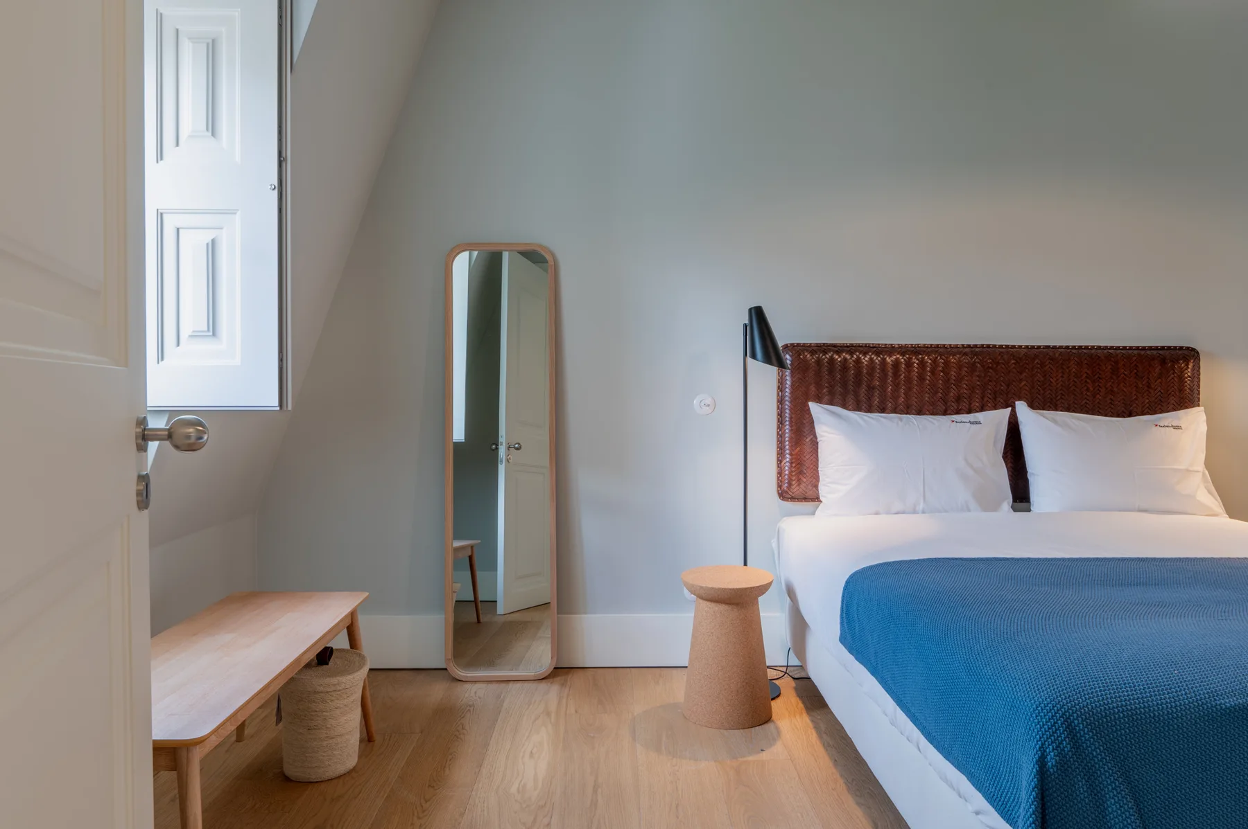 A bedroom with a bed dressed in white and blue bedding beside a full-length mirror.
