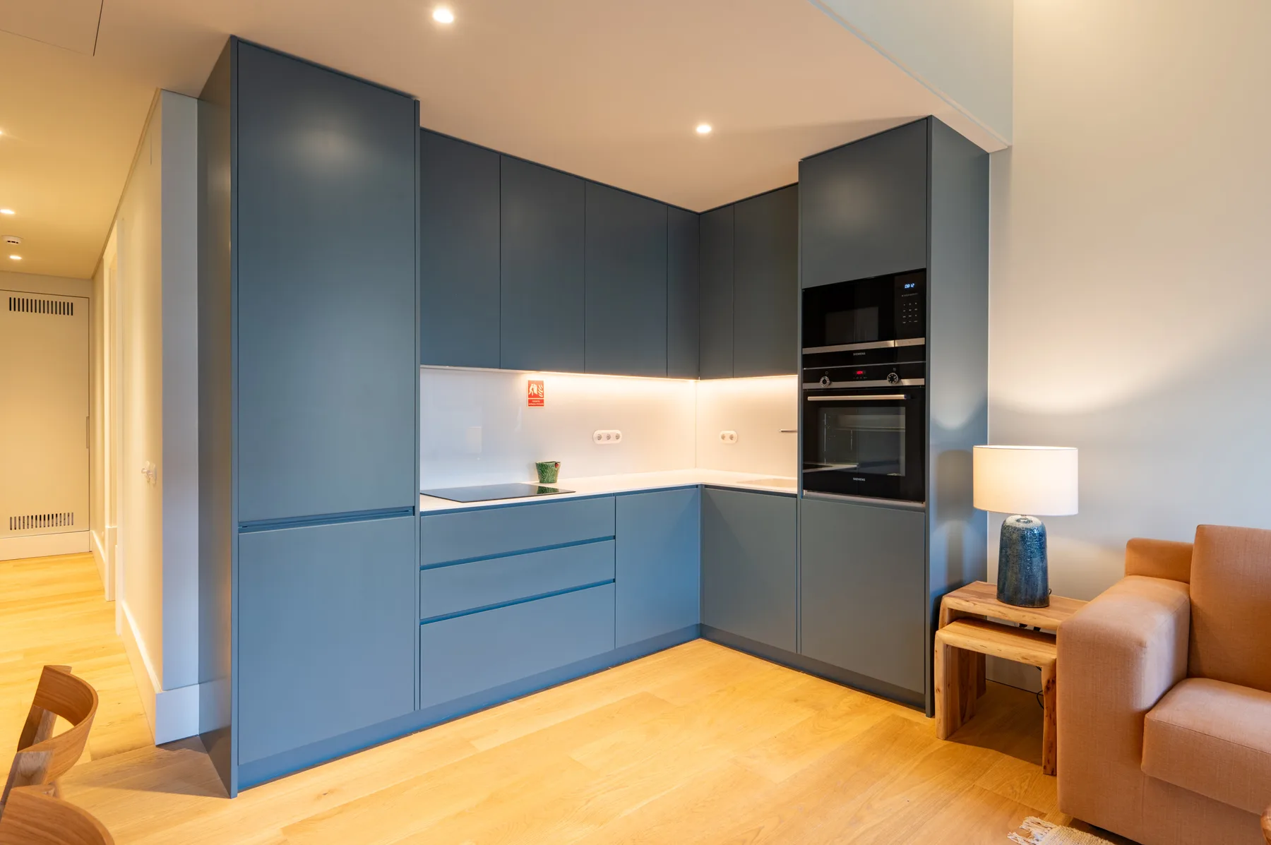 A modern kitchen with blue cabinetry and a light wood floor.
