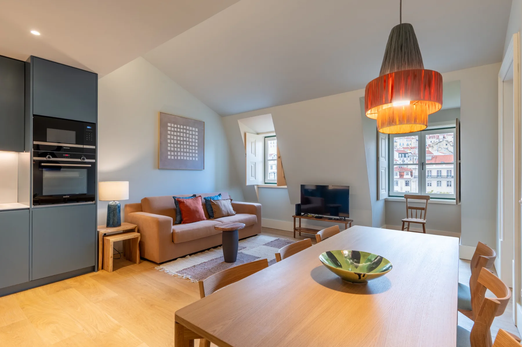 Living and dining area with seating, a television, and a table beside the windows.