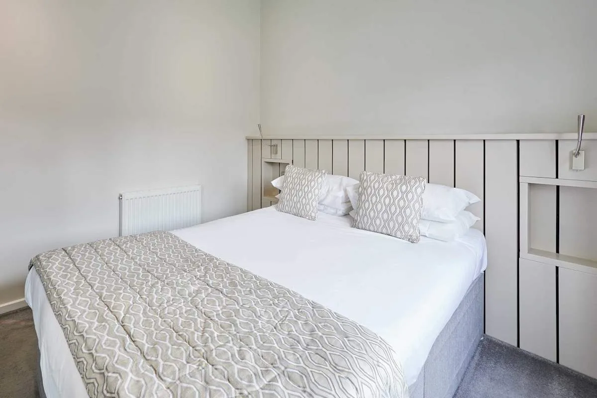 A bedroom with a neatly made bed and patterned cushions.