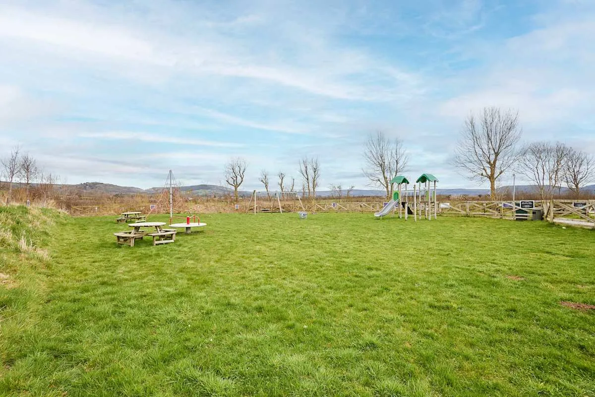 A grassy outdoor recreation area with picnic tables and a small playground.