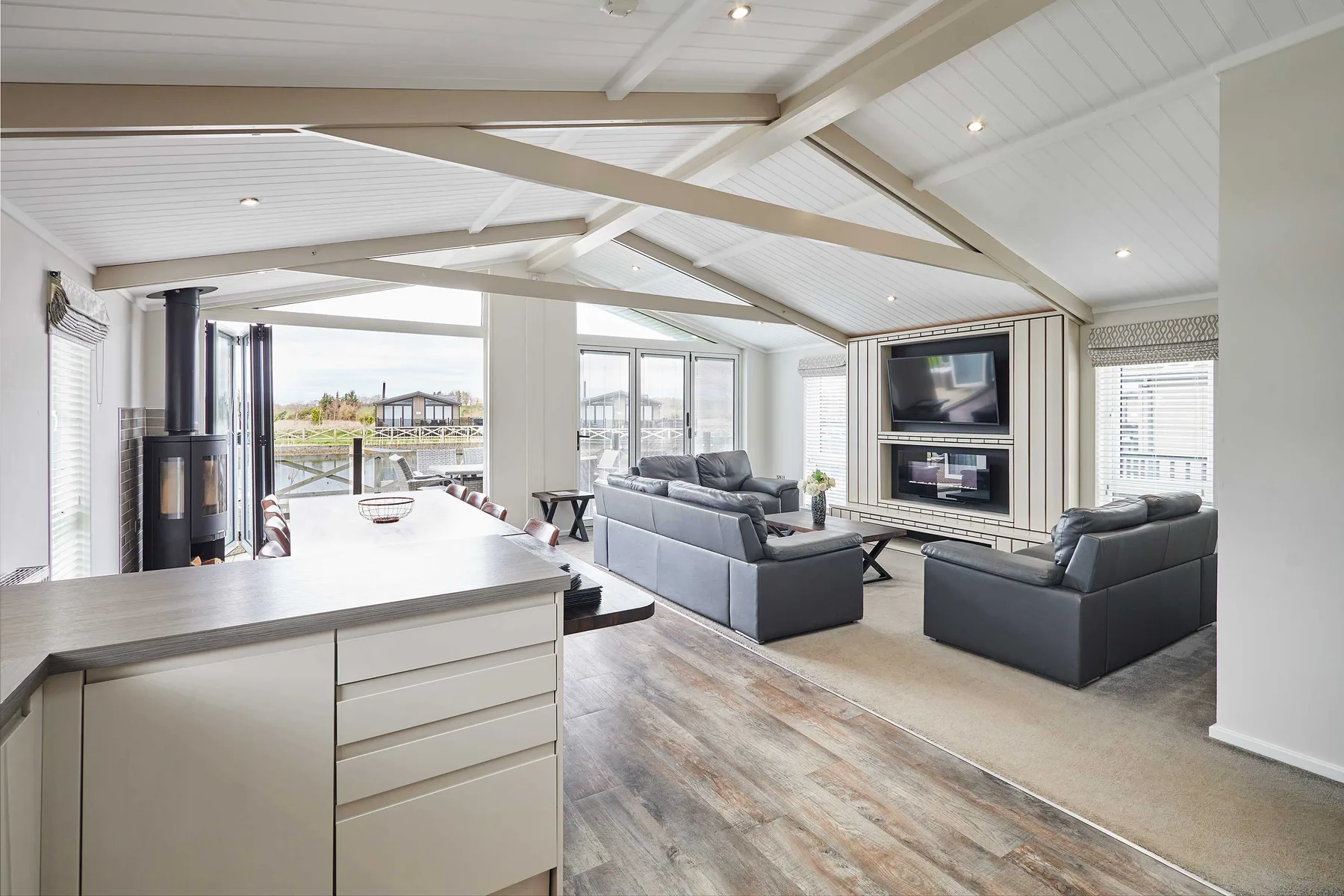 A bright open-plan living room with a kitchen counter, seating, and a television.