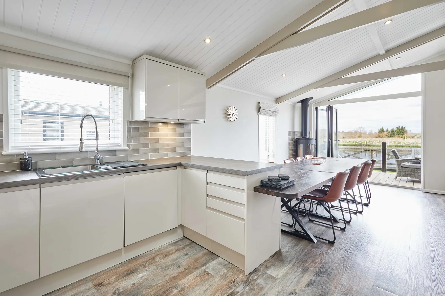 Una cocina luminosa se abre a un comedor con grandes ventanales y vistas al exterior.