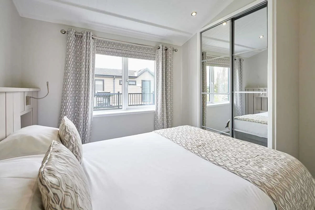 A bright bedroom with a large bed and mirrored wardrobe.