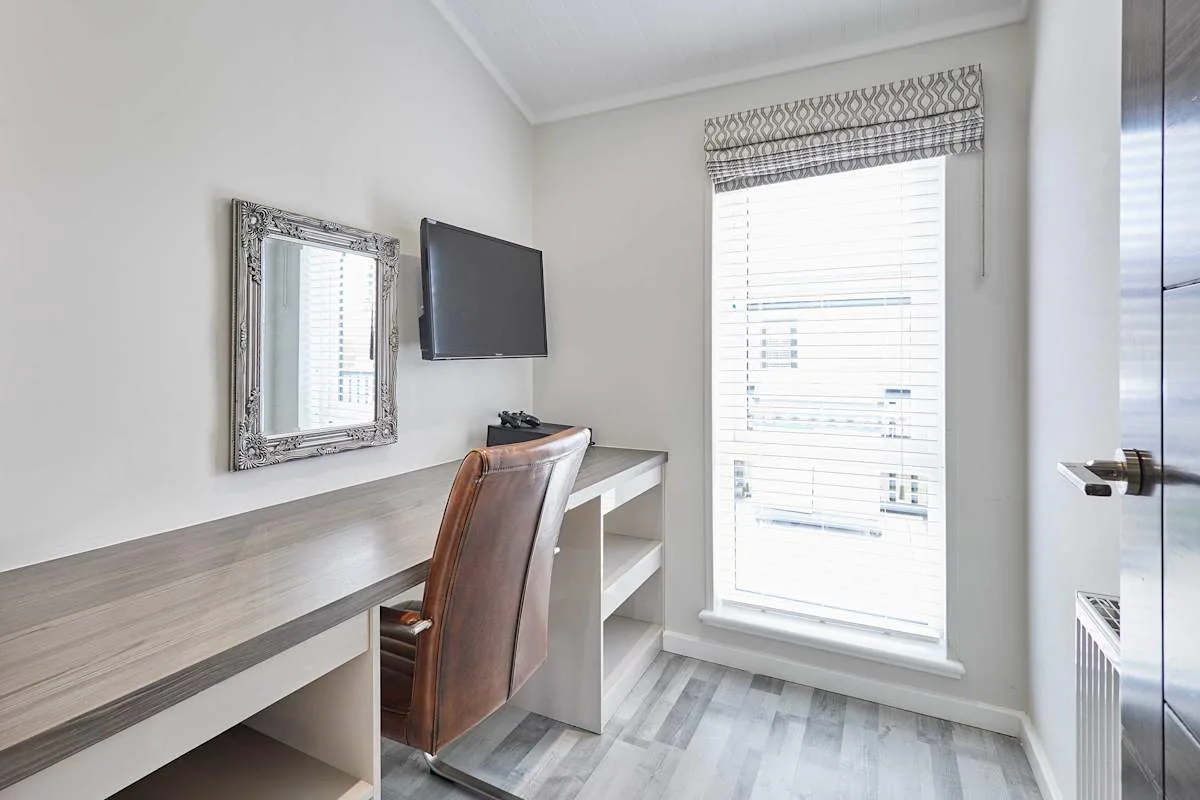 A bright desk area with a chair, wall-mounted television, and window.