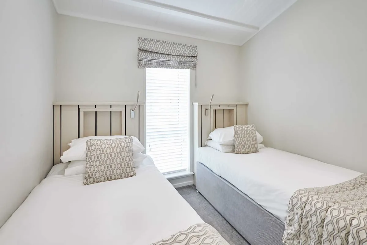 A bright twin bedroom with two beds and a window between them.
