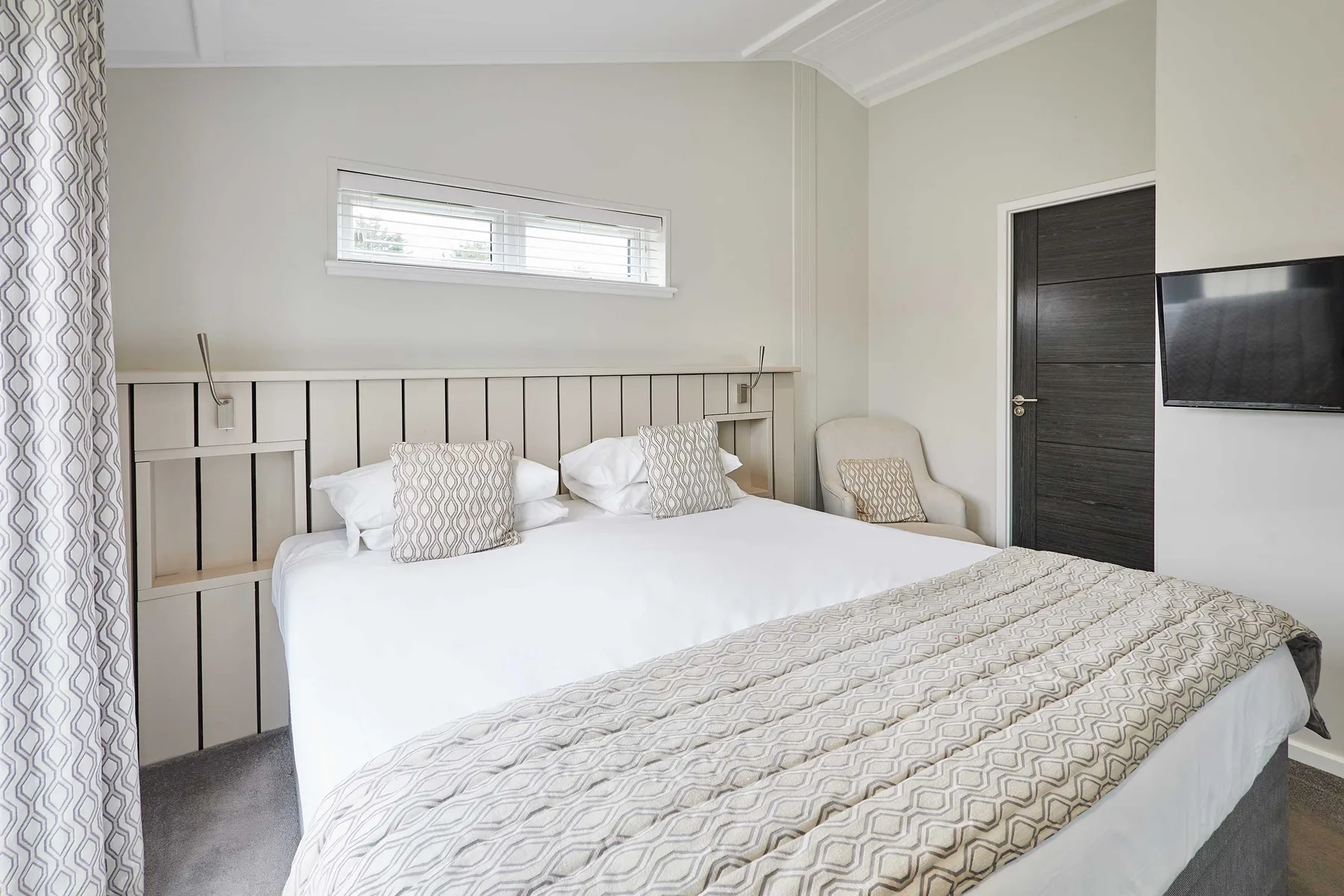 A bedroom with a neatly made bed and a wall-mounted television.