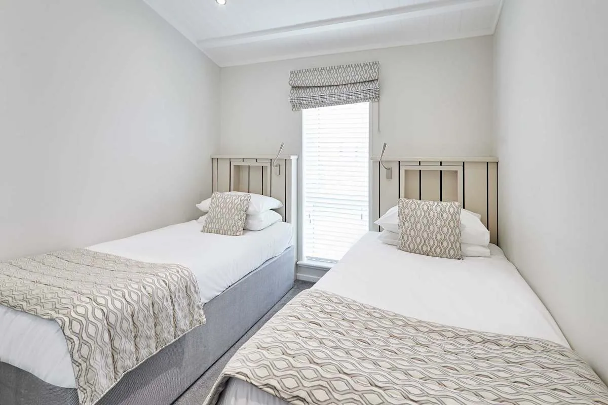 A bedroom with two beds and a window between them.