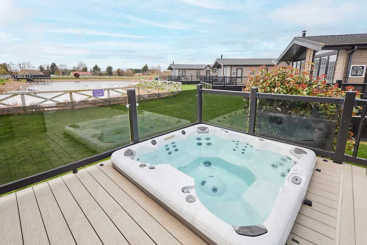 An outdoor hot tub sits on a wooden deck beside a glass railing.