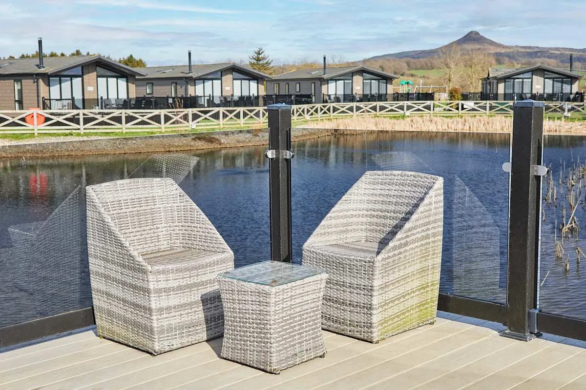 Outdoor seating overlooks a pond, with lodge buildings and hills in the background.
