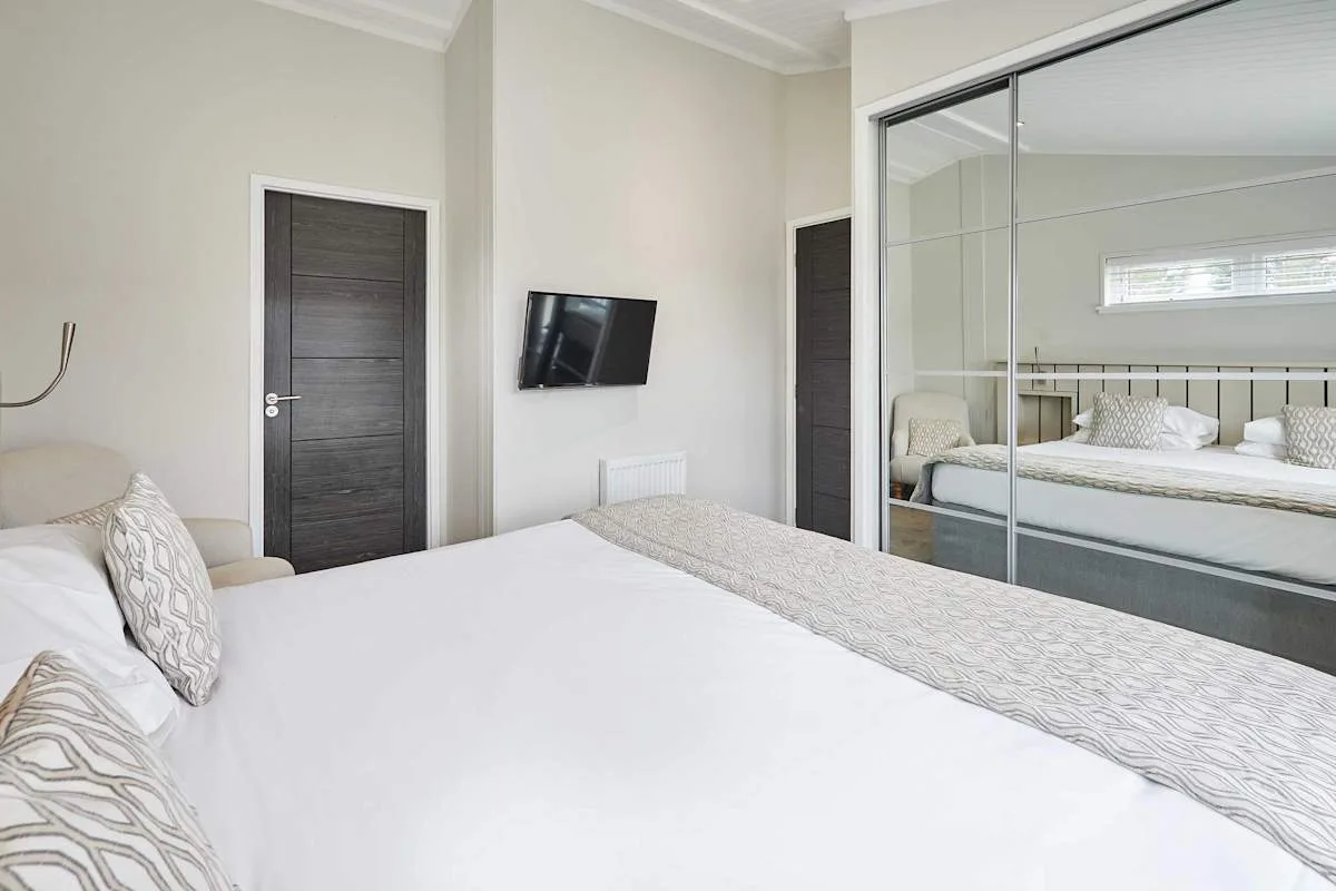 A bright bedroom with a large bed and mirrored wardrobe doors.