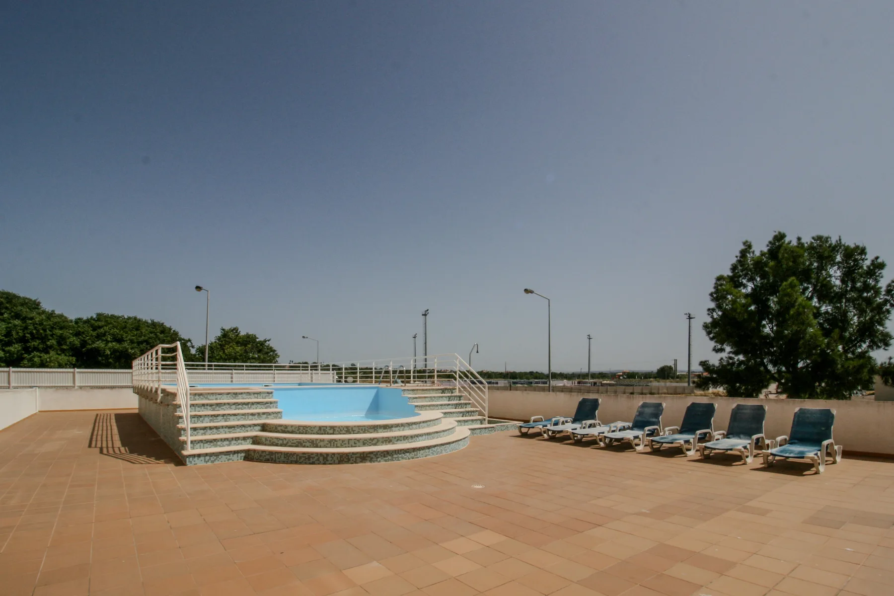 Una piscina en la azotea y una terraza de baldosas con asientos bajo un cielo despejado.