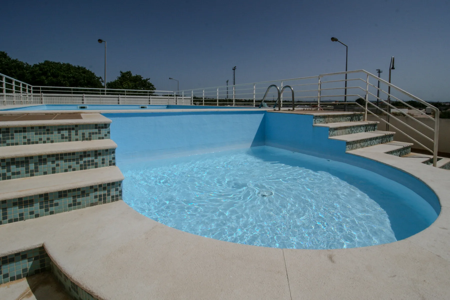 Una piscina al aire libre con escalones revestidos de azulejos y barandillas metálicas.