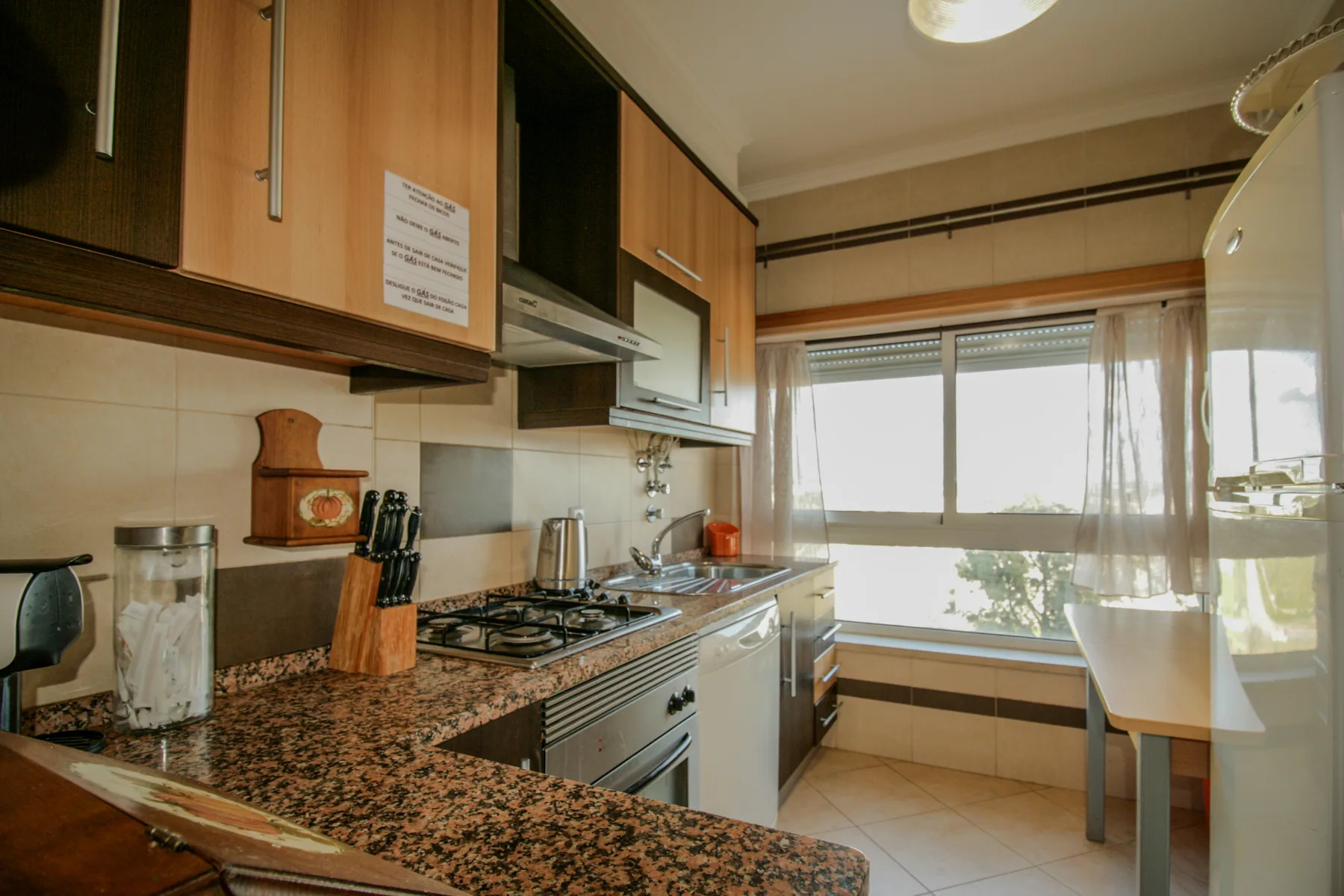Una cocina con gabinetes de madera y una encimera da a una luminosa zona de comedor con ventanas.