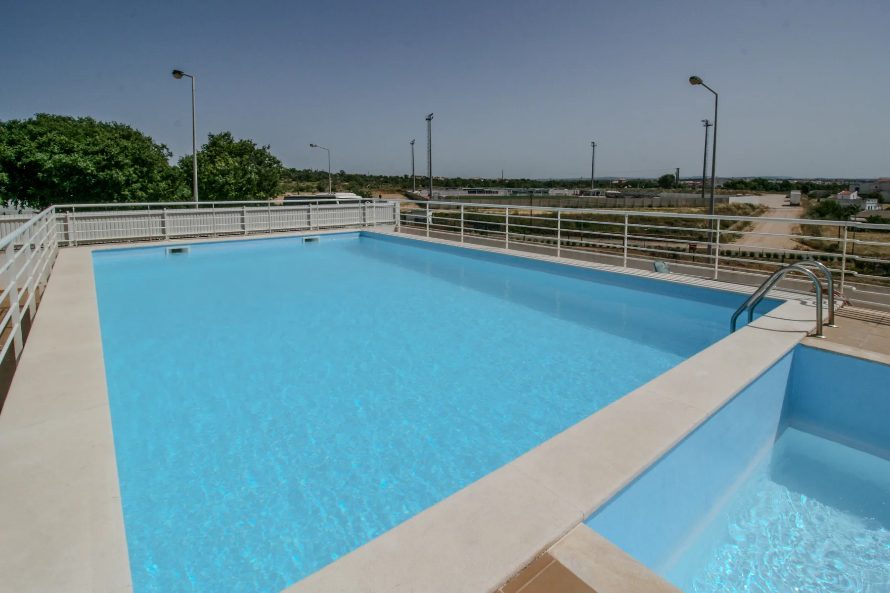 An outdoor swimming pool with pale stone coping and metal railings.