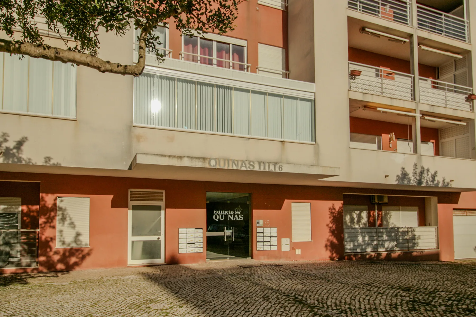 Exterior de un edificio de apartamentos con balcones y una entrada pavimentada.