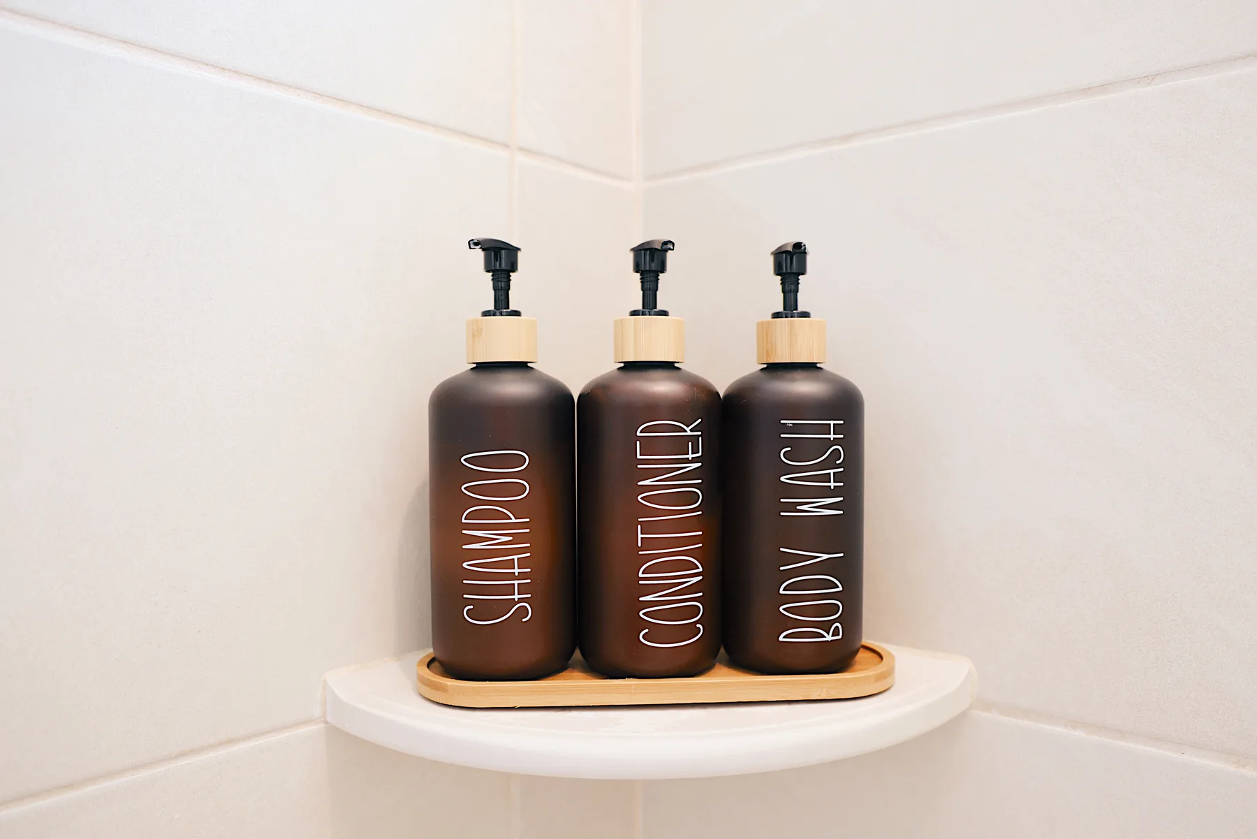 Tres botellas con dosificador de champú, acondicionador y gel corporal están sobre una repisa de baño.