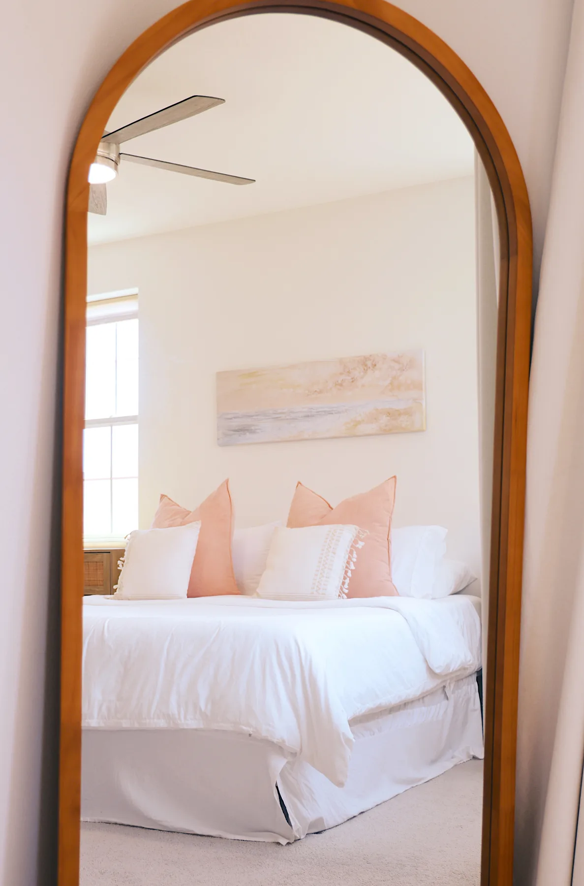 Un dormitorio luminoso con una cama bien tendida y un paisaje enmarcado encima.