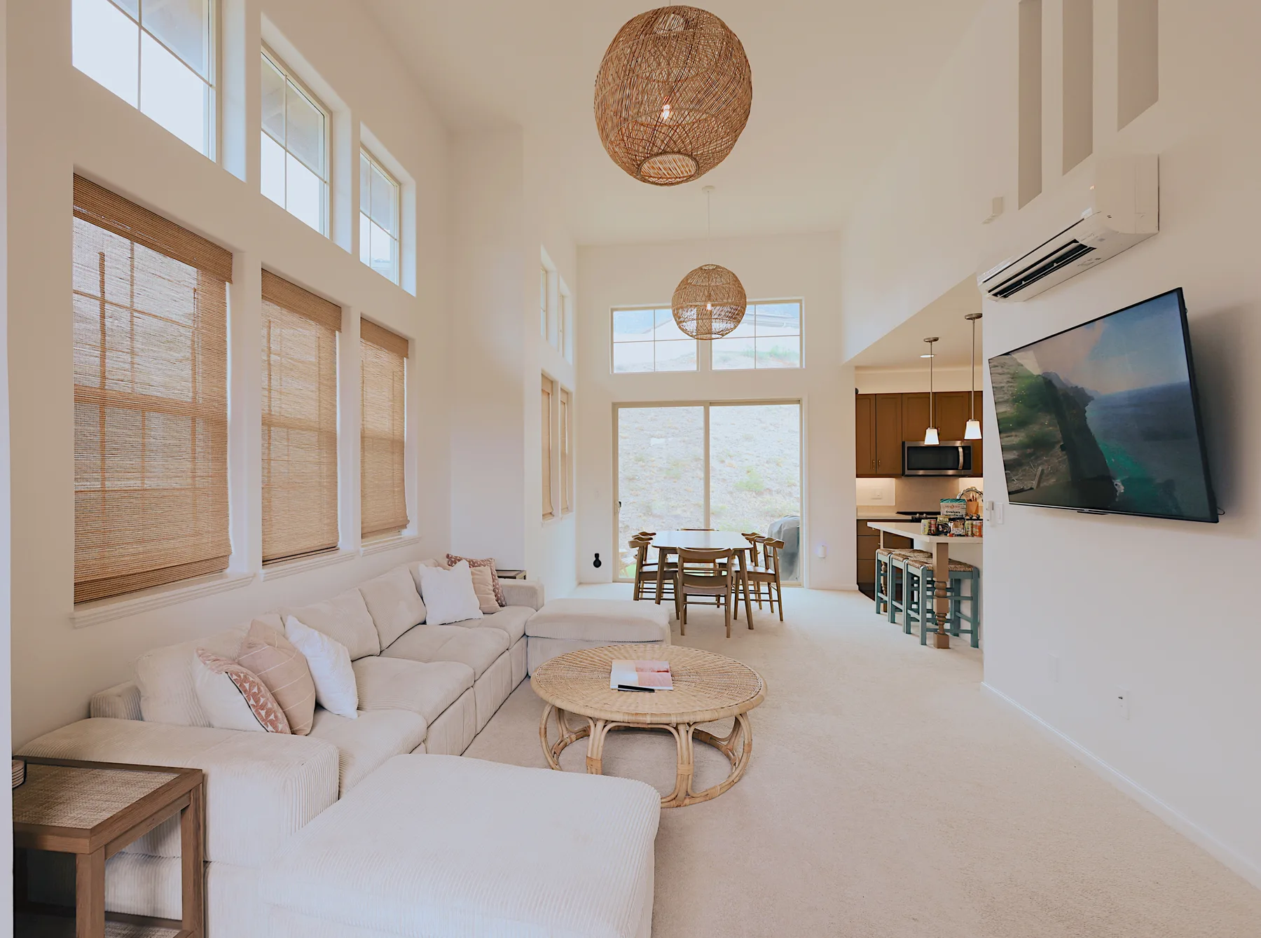 A bright living room opens onto a dining area, with a sectional seating area and large windows.