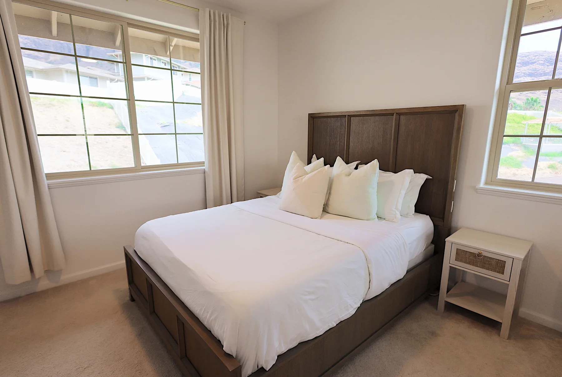 Un dormitorio con una cama vestida con ropa blanca entre dos ventanas.