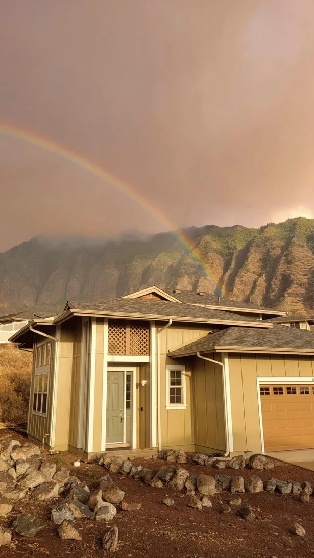 Una casa se encuentra en un paisaje rocoso bajo un arcoíris y una cordillera.