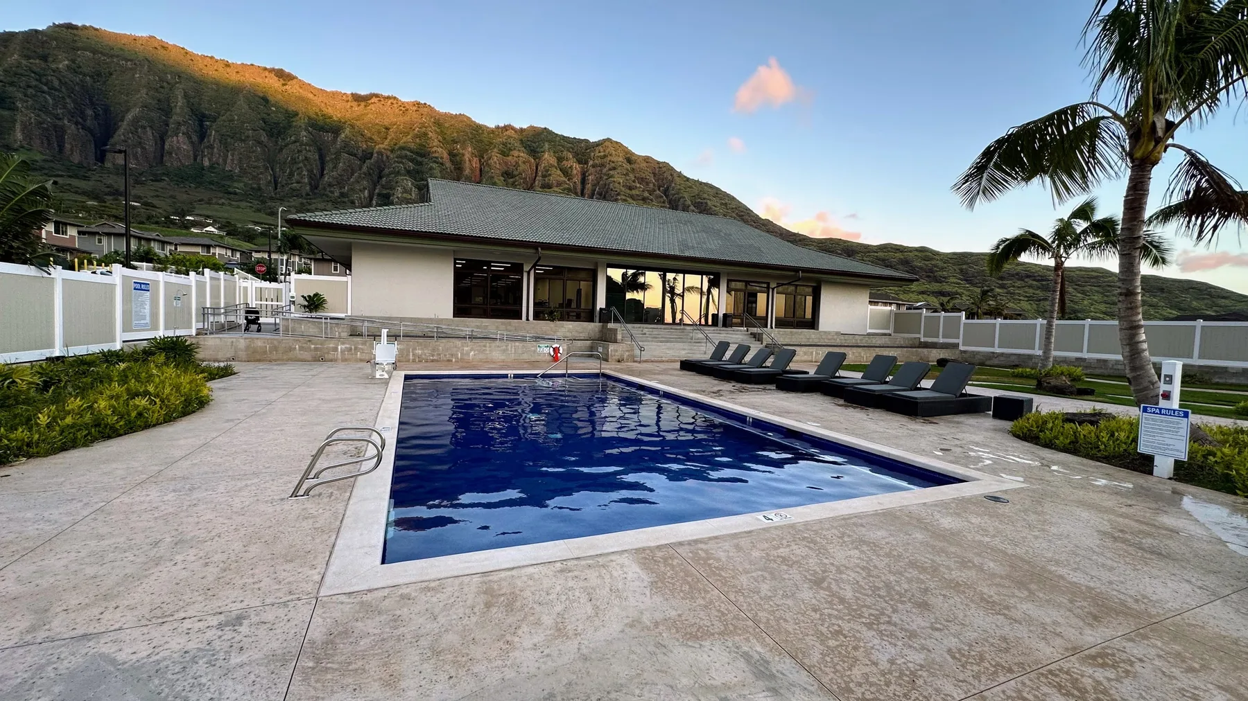 Una piscina al aire libre está junto a un pabellón cubierto, con colinas verdes al fondo.