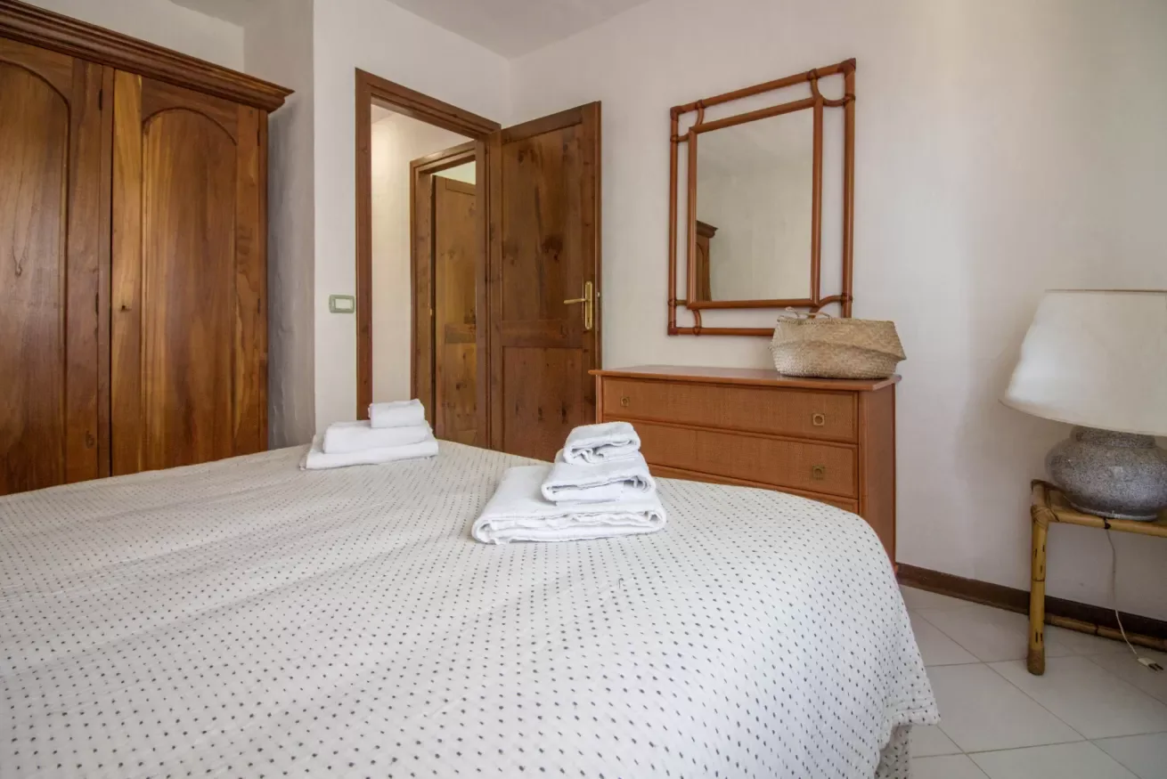 A bedroom with a bed, wooden wardrobe, dresser, and wall mirror.