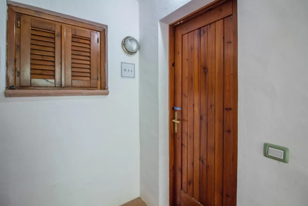 A white-walled interior with a wooden door and shuttered window.