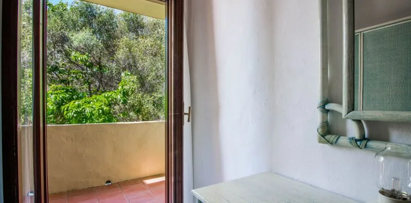 A room opens onto a balcony with green trees visible outside.