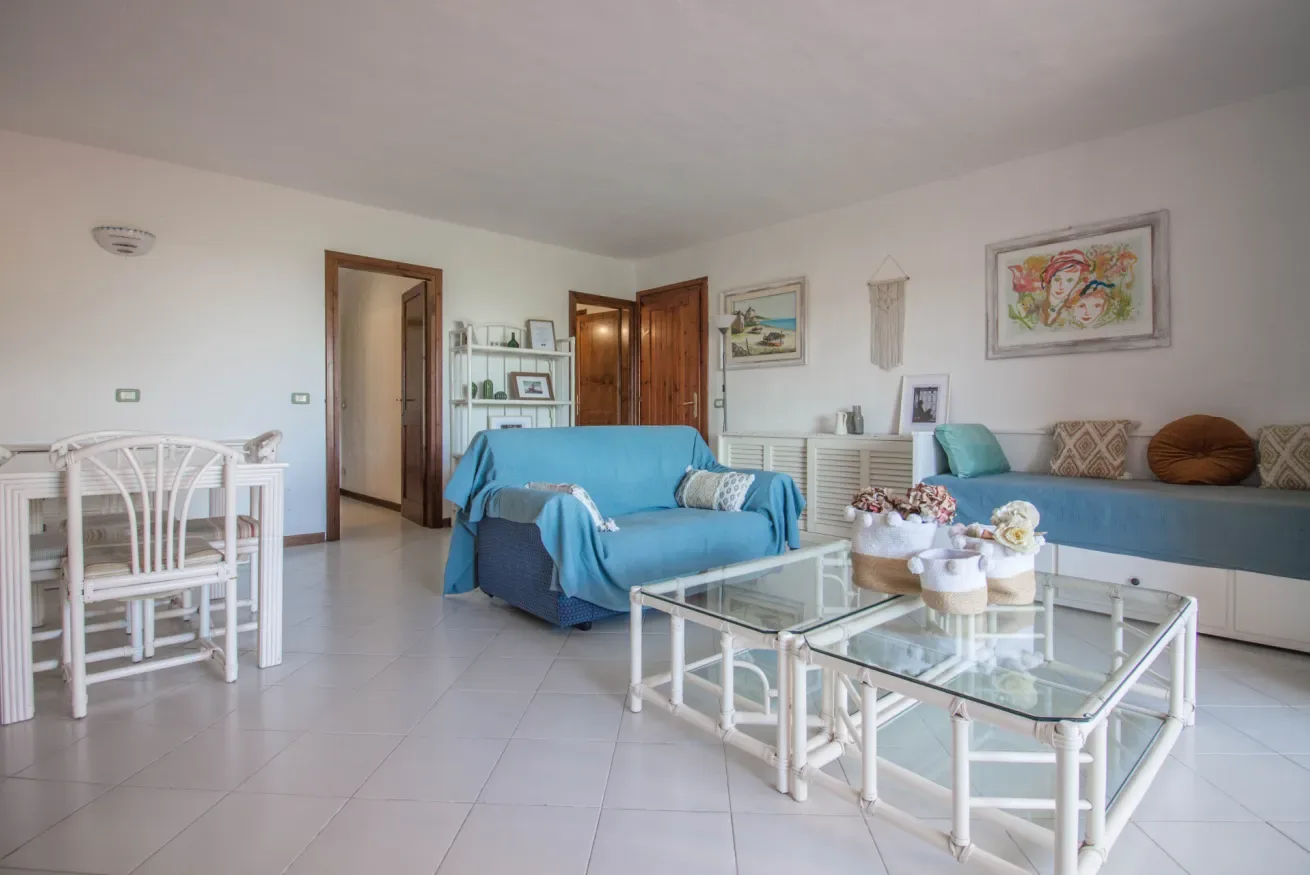 A bright living room with blue seating, a glass coffee table, and a dining area.
