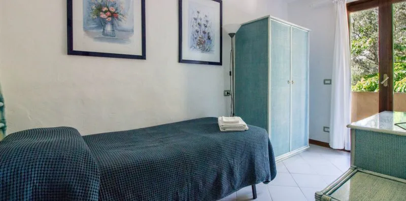 A bedroom with a bed, a wardrobe, and a glass door opening to greenery.