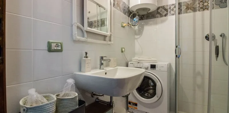 A tiled bathroom with a sink, washing machine, and glass shower.