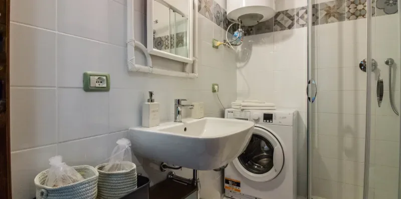 A tiled bathroom with a sink, washing machine, and glass shower.