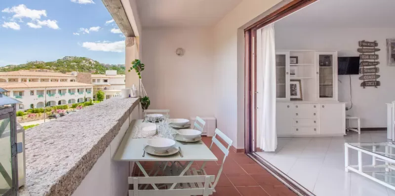A balcony dining area opens onto a bright interior with white furnishings.