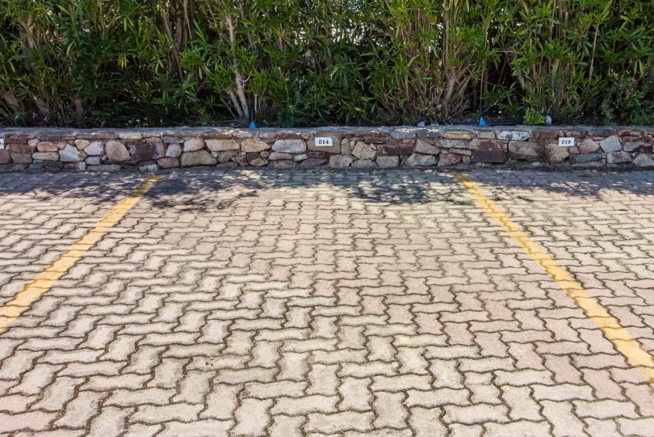 A paved parking area with yellow lines and a stone wall backed by greenery.