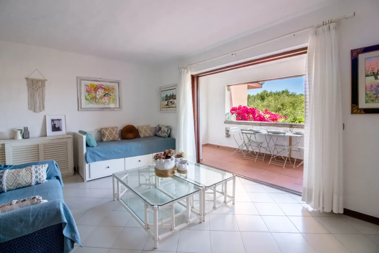 A bright living room opens onto a terrace with a small table and chairs.