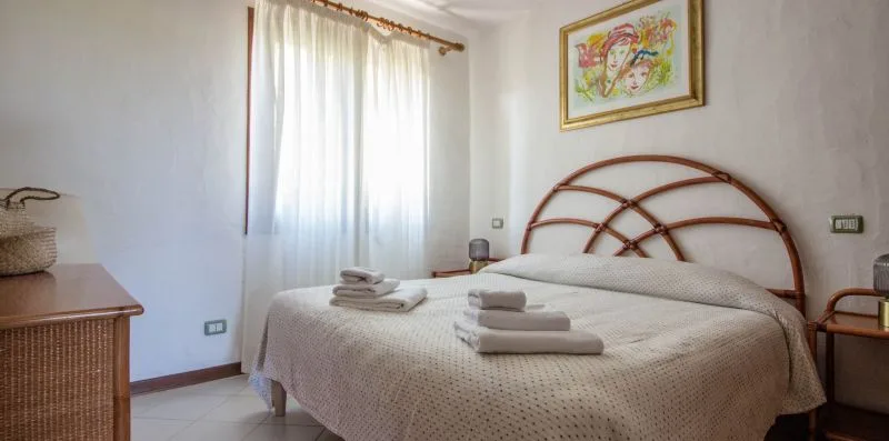 Un dormitorio con una cama, toallas dobladas y una ventana luminosa con cortinas.
