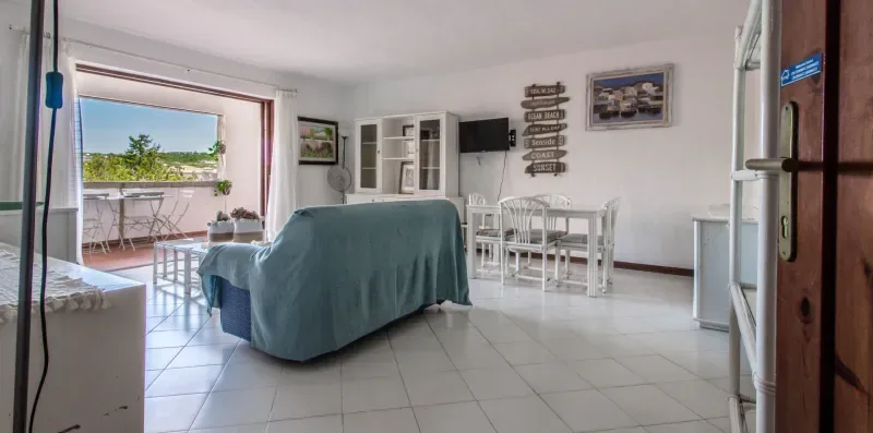 A bright living room with seating, a dining table, and an open balcony door.