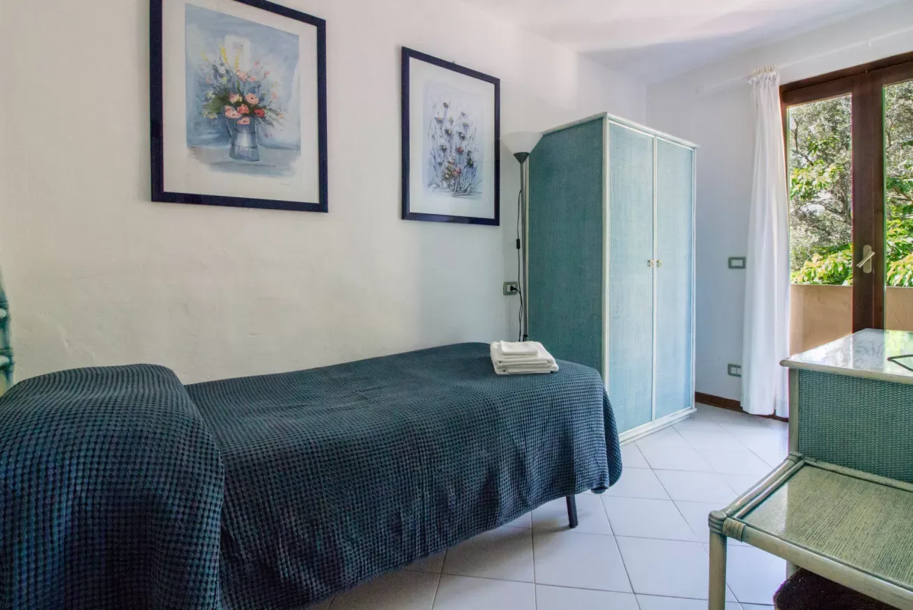A bedroom with a bed, framed artwork, and a glass door opening onto greenery.