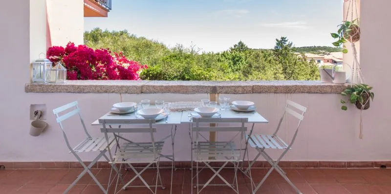 Una pequeña zona de comedor con mesa y sillas plegables da a un paisaje frondoso.