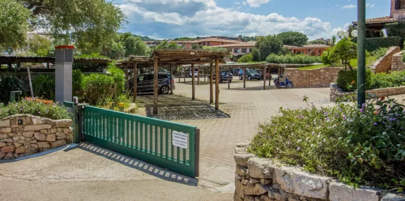 An outdoor entrance with a green gate, paved drive, and landscaped stone borders.