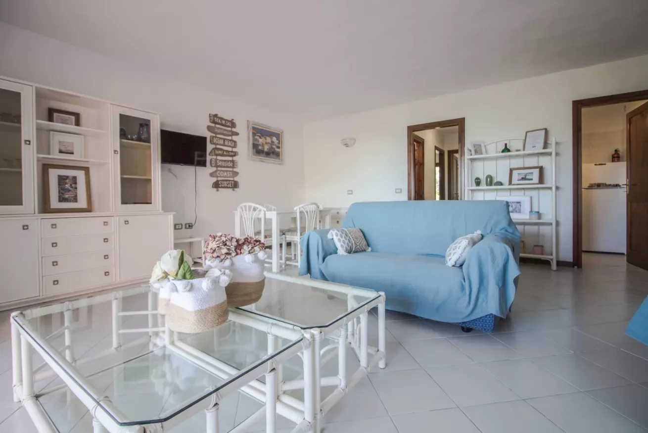 A bright living room with blue seating, glass tables, and open shelving.