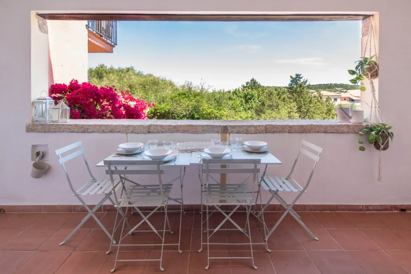 A dining area with a table and chairs faces a wide window overlooking greenery.