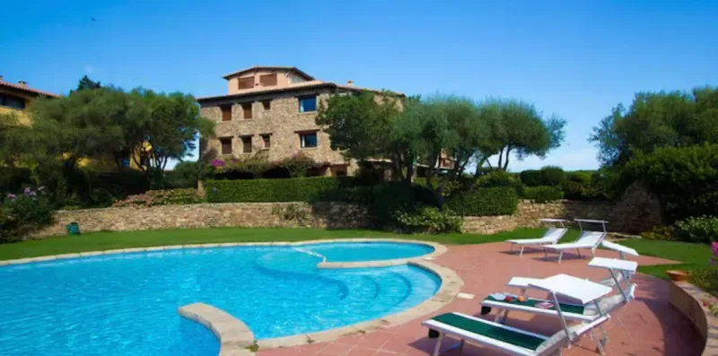 An outdoor swimming pool beside a stone building and landscaped grounds.
