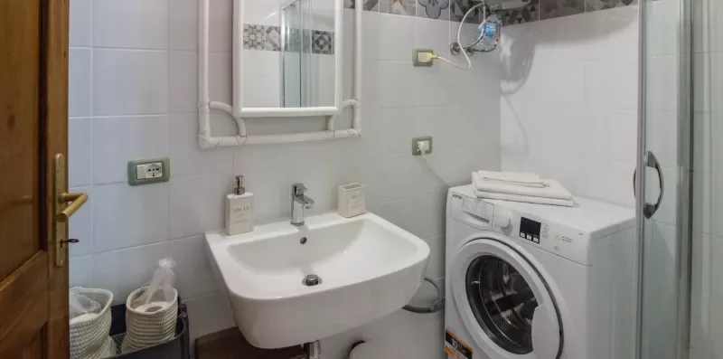 A tiled bathroom with a sink, washing machine, and glass shower.