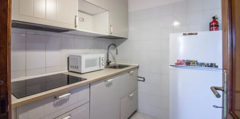 A tiled kitchen with a countertop, cooktop, and refrigerator.