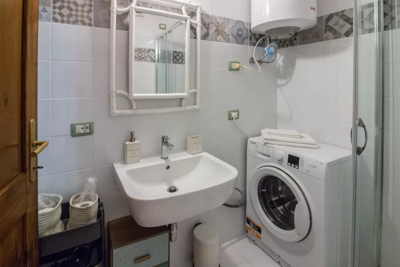 A tiled bathroom with a sink, washing machine, and glass shower.